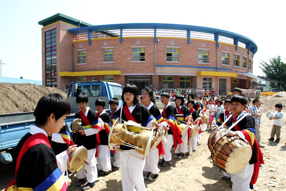 삼우초풍물패 학생들이 지난 3일 이 학교에서 열린 ‘2006 풍년기원 단오맞이 한마당’ 행사에서 개회식에 앞서 길굿을 벌이고 있다. 운동장 고르기가 끝나지 않아 한 켠에 흙더미가 쌓여 있지만 지난 5월 완공되어 이날 모습을 드러낸 학교 건물에는 학생 중심, 지역 사회와의 소통이라는 삼우초등학교의 철학이 고스란히 담겨 있다.