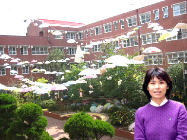 학교 건물사이에 설치한 철사줄에 학생들이 여러가지 빛깔로 색칠한 우산과 한지로 만든 물고기 모형이 내걸려 있다. 사진 속의 인물은 강정숙 교사. 군산동고 제공