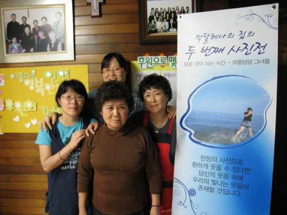프리랜서 사진작가 김정하(맨 왼쪽)씨 등 막달레나의 집 사진전 참여자들이 홍보 포스터 앞에서 웃음을 짓고 있다.
