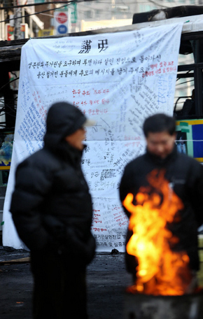서울 용산구 한강로3가 철거민 참사 현장에 마련된 합동분향소 인근에서 전국철거민연합 회원들이 불을 피우며 추위를 쫓고 있다. 뒤로 참사 현장 접근을 막았던 경찰 차량에, 시민들이 희생자들을 추모하는 글을 적은 현수막이 걸려 있다. 정용일 기자 yongil@hani.co.kr