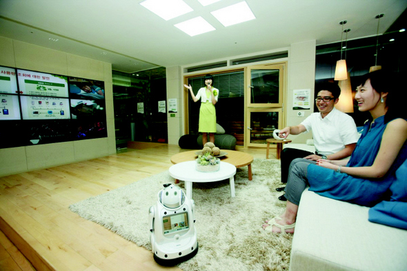 서울 역삼동 푸르지오 밸리 주택문화관을 찾은 사람들이 본보기집 거실에 앉아서 대형 모니터와 로봇이 알려주는 주택의 실시간 에너지 사용량을 보고 있다.  대우건설 제공