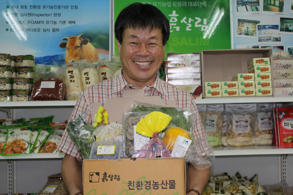 이태근 회장이 매주 도시의 가정으로 직배달하는 흙살림의 유기농산물꾸러미를 들고 활짝 웃고 있다. 