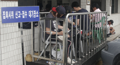 지난 12일 서울 서초경찰서 집회신고 접수 장소 앞에서 현대기아차 쪽 아르바이트 학생 등이 음악을 듣거나 만화책을 보며 줄을 서서 대기하고 있다. 맨 뒤에 고개를 숙이고 앉아있는 이가 동희오토 조합원 박성영씨다.  동희오토사내하청지회 제공