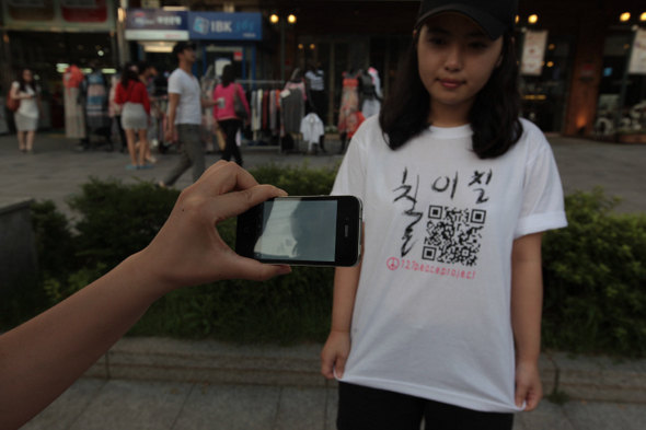 한 시민이 ‘칠이칠’이라는 로고가 디자인된 티셔츠를 스마트폰으로 찍고 있다. 티셔츠에 있는 큐아르(QR)코드를 찍어 인터넷에 접속하면 평화 메시지를 담은 동영상이 나온다.  7·27프로젝트팀 제공