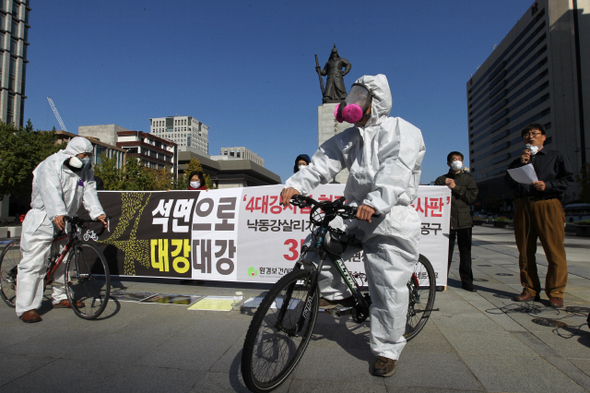 한국석면추방네트워크와 환경보건시민센터 등 환경·사회 단체 소속 회원들이 25일 오전 서울 세종로 광화문광장에서 4대강 현장의 석면조사보고서를 발표하며 방진복에 방진마스크를 쓴 채 자전거를 타는 행위극을 하고 있다.  류우종 기자wjryu@hani.co.kr