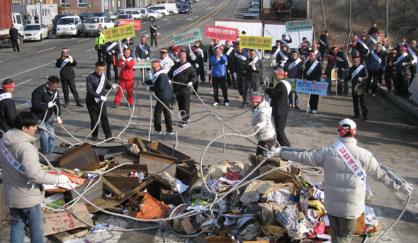 12일 오전 경기 화성시 남양동 화성시청 옆에서 고물상 관련 회원들이 화성시의 고물상 입지 규제를 강화하는 지침을 입법예고한 것에 반발해 폐지와 고철을 도로 위에 쏟아놓고 끈으로 옥죄는 퍼포먼스를 하고 있다.