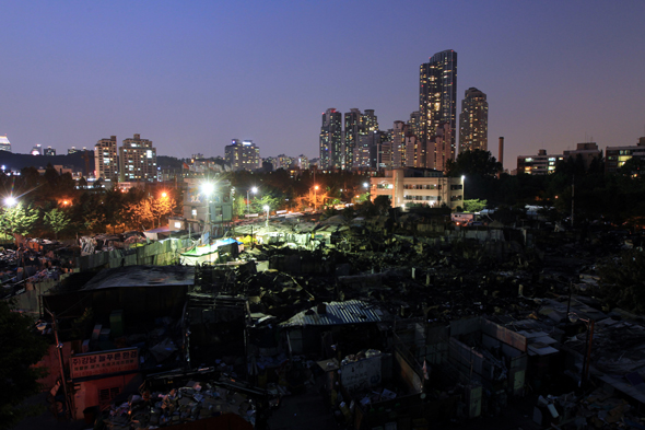 지난해 6월 폐기물 야적장에 난 불로 잿더미가 된 서울 강남구 포이동 1226번지 재건마을에 내려앉은 어둠 뒤로 타워팰리스 등 고층 주상복합건물이 불빛을 뽐내고 있다. 신소영 기자 viator@hani.co.kr