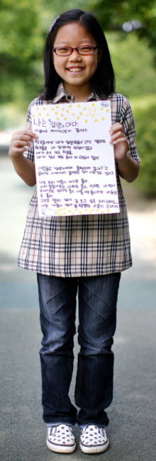 한국입양홍보회가 입양을 홍보하기 위해서 2009년에 연 행사에서 한 아이가 입양된 자신의 이야기를 담은 손팻말을 들고 활짝 웃고 있다.  사진작가 박찬학씨 제공
