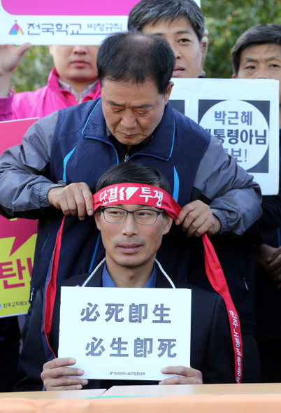 주봉희 민주노총 부위원장이 24일 오후 서울 세종로 정부서울청사 앞에서 열린 전교조 설립 취소 통보 항의 기자회견에서 김정훈 전국교직원노동조합 위원장에게 ‘단결 투쟁’이라고 적힌 붉은 머리띠를 매어 주고 있다.  김태형 기자 xogdu555@hani.co.kr