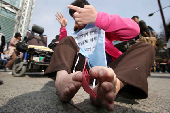 26일 오후 서울 종로구 보신각 앞에서 열린 ‘부양의무제 폐지, 기초법 개악 저지 최옥란 열사 정신계승 3·26 빈민대회’에서 한 장애인 참가자가 복지 확대의 염원을 담아 발로 희망의 종이배를 접고 있다. 이날 참가자들은 정부가 정한 장애인의 날(4월20일)을 장애인 차별 철폐의 날로 바꾸고, 장애등급제와 부양의무제를 폐지할 것을 주장했다.  류우종 기자 wjryu@hani.co.kr