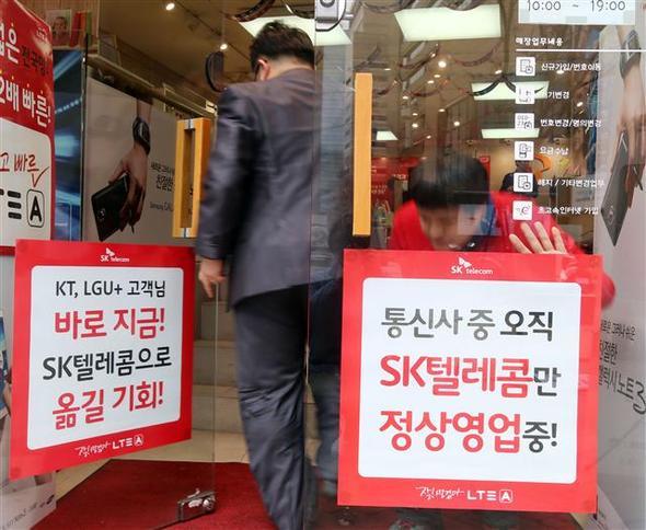 이동통신사별로 영업정지가 시작된 3월13일 서울 중구 명동 에스케이텔레콤(SKT) 이동통신 판매점 직원이 정상영업을 안내하는 홍보물을 출입문에 부착하고 있다. 뉴스1, 연합뉴스
