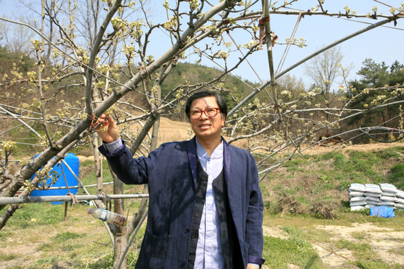 신명식씨가 자신이 일하는 유기농 배 밭에서 개량한복을 입고 환한 표정을 짓고 있다.