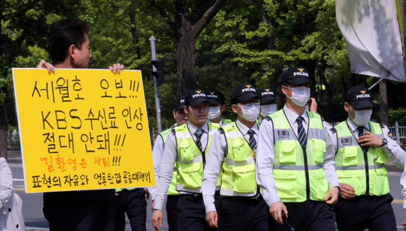 12일 오후 서울 여의도 한국방송 본관 앞에서 수신료 인상 반대 손팻말을 들고 1인시위를 벌이는 ‘표현의 자유와 언론탄압 공동대책위원회’ 소속 한 회원 옆으로 경찰이 지나가고 있다. 이정용 기자 lee312@hani.co.kr