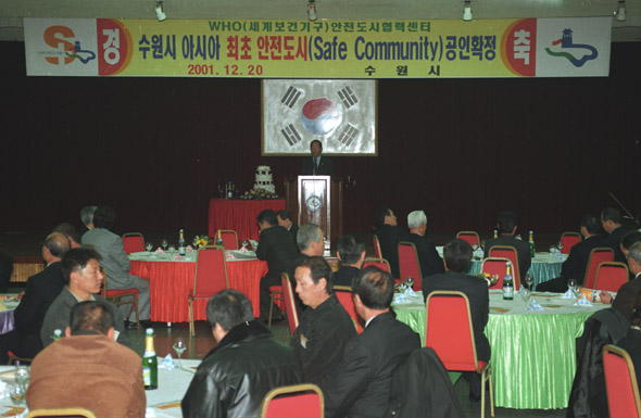 2001년 12월 20일 고 심재덕 전 수원시장이 세계보건기구(WHO)로부터 수원시의 아시아 최초 안전도시 공인 확정을 기념하는 경축식에서 축사를 하고 있다. 최근 수원시장 선거에 나선 새누리당 김용서 후보가 자신의 시장 역임 시절인 2002년 대한민국 최초로 국제안전도시 인증을 받았다고 밝히자 심 전 시장의 유족은 거짓말이라며 이 사진을 증거로 제시했다. (사진제공 고 심재덕 전 수원시장의 유족)
