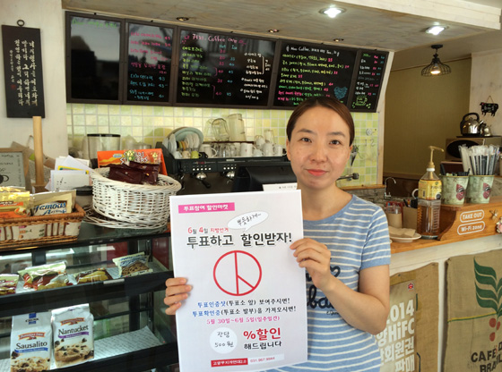 경기도 고양시청 앞 커피숍 ‘시티힐’ 주이숙 대표가 6·4 지방선거 투표에 참여한 유권자에게 커피 값을 500원씩 깎아주겠다는 ‘투표참여 할인마켓’ 안내판을 들고 있다. 고양무지개연대 2.0 제공