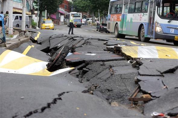 26일 전날 내린 집중호우로 부산 북구 구포3동 공영주차장 내리막길에 1차선 도로 50ｍ가 구겨진 모양으로 움푹 내려앉아 경찰이 교통을 통제하고 있다. 부산/연합뉴스
