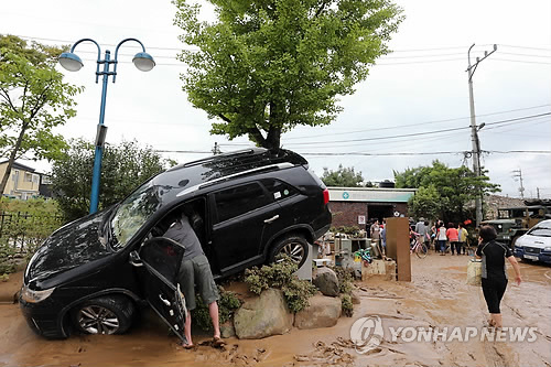기록적인 폭우로 침수피해를 입은 부산 기장군 장안읍사무소 앞에서 26일 침수차량에 대한 견인작업이 벌어지고 있는 가운데 화단에 걸친 차량 소유자가 물품을 챙기고 있다.(부산=연합뉴스)