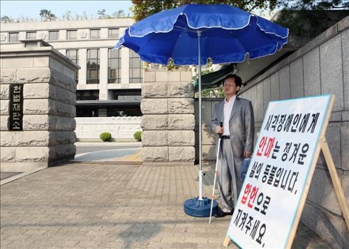 5월 7일 오전 서울 종로구 재동 헌법재판소 정문 앞에 설치된 이동식 차양막(파라솔)에서 시민들이 1인 시위를 하고 있다. 박한철 신임 헌법재판소장은 “사회적 약자의 1인 시위를 배려하기 위해 비와 햇볕을 피하도록 차양 시설을 마련하라”고 지시했다. 2013. 5. 7. 연합(사진 헌법재판소 제공)