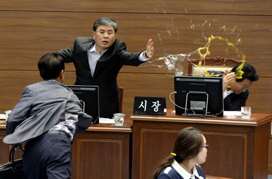 지난달 16일 경남 창원시 창원시의회 본회의장에서 김성일(왼쪽) 창원시의원이 프로야구 엔씨(NC) 다이노스 구단 전용구장 후보지 이전을 결정한 안상수(오른쪽) 창원시장에게 날달걀을 던지고 있다. 박재현(가운데) 창원시 제1부시장이 팔을 뻗어 막았으나, 안 시장은 2개의 달걀 가운데 첫번째 달걀을 오른팔에 맞았다.  경남신문 제공