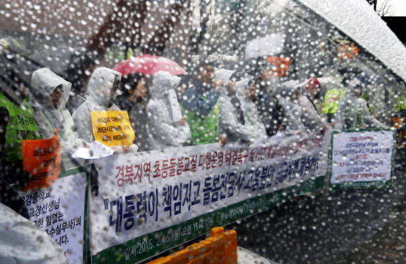 <b>빗발속 “대통령이 나서라”</b> 민주노총 공공운수노조 전국교육공무직본부 조합원들과 경북지역 초등돌봄교실 파업참가자가 16일 오전 서울 종로구 청운동 청와대 들머리에서 경북지역 초등돌봄교실 파행운영 및 돌봄전담사의 고용 불안, 임금 차별 등을 해결하라고 대통령한테 촉구하고 있다. 사진은 비가 내리는 가운데 한 참가자가 쓰고 있는 투명 우산을 통해 보이는 기자회견 모습이다. 이종근 기자 root2@hani.co.kr