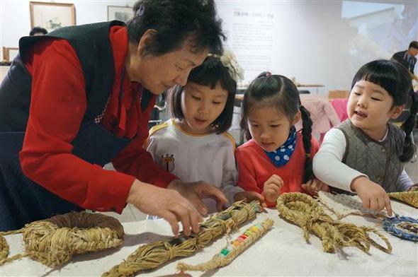 지난 12일 서울시 종로구 서울노인복지센터 1층 탑골미술관에서 ‘이상한 실험실’ 행사가 펼쳐졌다. 자원봉사자로 참여한 한인덕씨가 둥근달어린이집 어린이들에게 짚풀로 만든 달걀 꾸러미를 설명하고 있다.  서울노인복지센터 제공