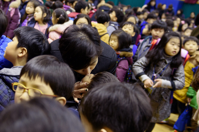 “이제 학부모님들은 밖으로 나가 주십시오”라는 안내 방송이 나왔다. 하나밖에 없는, 게다가 반쪽만 열린 강당 문을 빠져나가느라 일대 혼잡을 이루고 있는 학부형들 행렬에서 갑자기 한 엄마가 빠져나오더니 아이에게 달려가 입을 맞춘다. 아이는 엄마의 마음을 알까? 모정은 언제나 뜨겁다. 2015년 3월3일. 서울 언북초등학교 첫 등교의 날. 
 견석기/사진가 