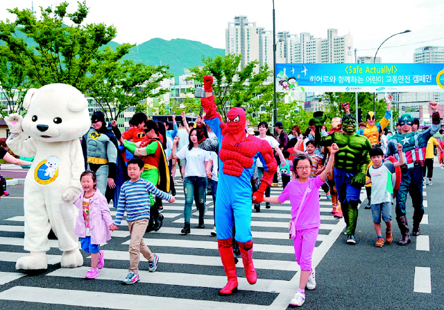 르노삼성자동차와 부산시가 지난 23일 부산시 부산진구 범전동 부산시민공원 앞 교차로에서 연 교통안전 거리 캠페인 행사에 참가한 어린이들이 스파이더맨 등 수퍼히어로 캐릭터로 분장한 도우미들의 손을 잡은 채 안전하게 건널목을 건너고 있다.  르노삼성자동차 제공 연합뉴스
