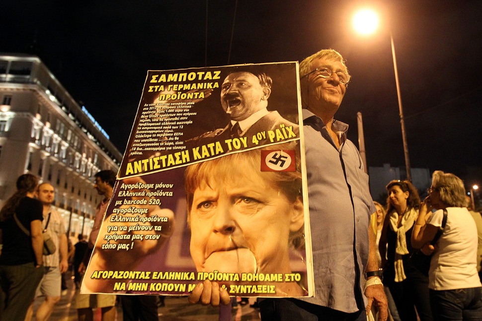 앙겔라 메르켈 독일 총리 방문을 하루 앞둔 2012년 10월8일 그리스 수도 아테네 의사당 앞에서 독일이 주도하는 그리스 구제금융에 반대하는 한 시민이 나치 독일의 지도자 아돌프 히틀러를 빗댄 메르켈 총리의 모습을 담은 포스터를 들고 있다. 그리스 노조가 주도한 이 시위에 등장한 이 포스터에는 “독일 제품 구매 거부, ‘제4제국’에 저항하자”라는 문구가 적혀 있다.