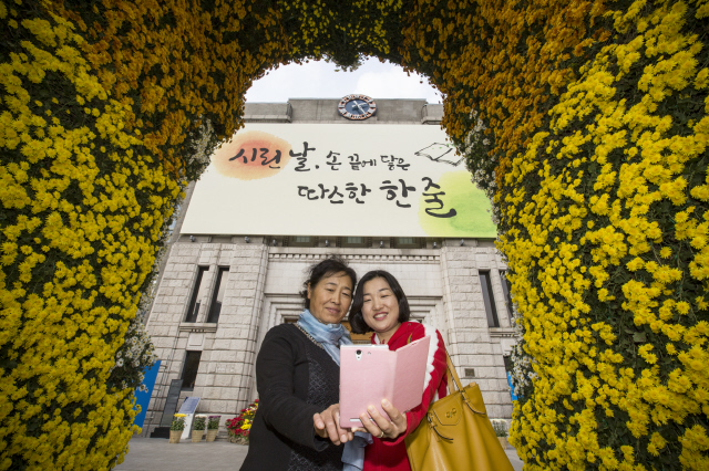 2일 오후 서울 중구 서울 도서관 외벽에 걸린 ‘시린 날, 손끝에 닿은 따스한 한 줄’이란 내용이 담긴 ‘꿈새김판’ 앞에서 관광객들이 기념촬영을 하고 있다. 꿈새김판에는 서울시가 공모전을 열어 뽑은 작품 가운데 우수작으로 선정된 안상선씨와 최예진씨의 작품을 합친 글귀를 적어놓았다.  김성광 기자 flysg2@hani.co.kr