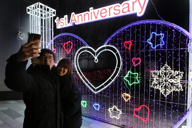  롯데몰은 수원점 개점 1주년과 연말을 기념하기 위해 약 두 달간 롯데물 1층 외부와 5층 스카이가든 등에서 ‘루미나리에 페스티벌’을 진행한다고 밝혔다. 롯데몰 수원점을 찾은 고객들이 지난달 30일 경기 수원시 권선구 서둔동 매장에 마련된 ‘루미나리에 하트존’에서 기념사진을 찍고 있다. 롯데자산개발 제공