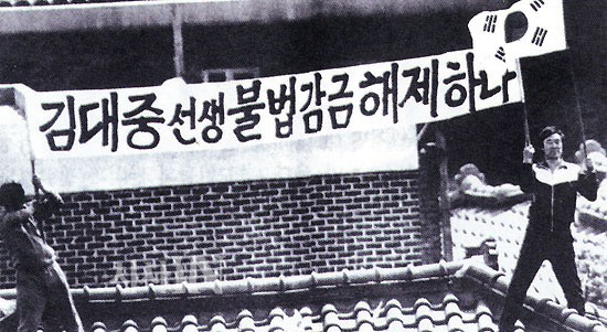 1985년 1월 미국 망명에서 돌아온 이래 87년 6월까지 2년 4개월 동안 이희호와 김대중은 55차례 동교동에서 가택연금을 당했다. 87년 4월부터는 직계가족만 출입이 가능했다. 5월1일 통일민주당 창당대회 참석도 막히자, 비서 김옥두(오른쪽)와 남궁진(왼쪽)이 이불 홑청으로 만든 천에 ‘김대중 선생 불법감금 해제하라’고 쓴 현수막과 태극기를 들고 동교동 지붕 위에서 시위를 하고 있다. 사진 김대중평화센터 제공