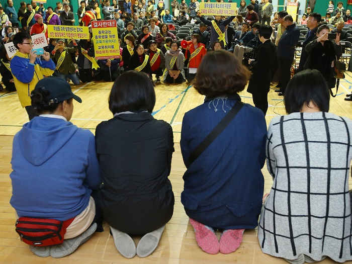 2015년 11월2일 서울 동대문구 성일중학교에서 장애인 가족들이 단상에서 무릎을 꿇고 '서울커리어월드' 설립을 호소하자, 설립을 반대하는 주민들도 무릎을 꿇고 자신들의 입장을 이야기하고 있다. 연합뉴스