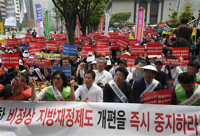 밖에선 23일 오후 서울 세종로 정부서울청사 별관 앞에서 열린 ‘지방재정 개악안 철회 촉구 경기도민 결의대회’에서 경기지역 6개시 시민들이 정부의 지방재정개편안에 반대하며 구호를 외치고 있다. 수원·용인·화성·과천·성남·고양 등 6개시는 재정 수요보다 수입이 많아 지방교부금을 받지 않는 ‘불교부단체’로, 개편안이 시행되면 시예산이 크게 줄어들게 된다며 반발하고 있다.  연합뉴스