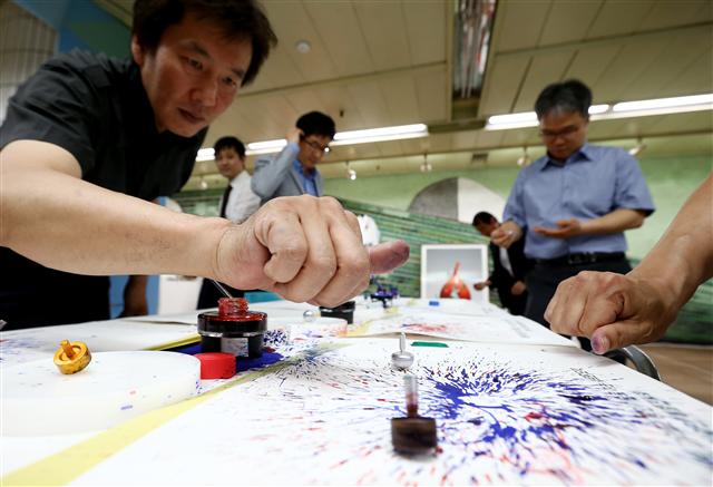 23일 오전 서울 성동구 5호선 왕십리역 지하 2층 대합실에서 열린 ‘숙련 기술인과 여성을 위한 취업박람회’에서 참가자들이 잉크가 담긴 팽이를 이용해 그림을 그리고 있다. 팽이는 문래동의 금속가공 기술인이 제작했다.  연합뉴스
