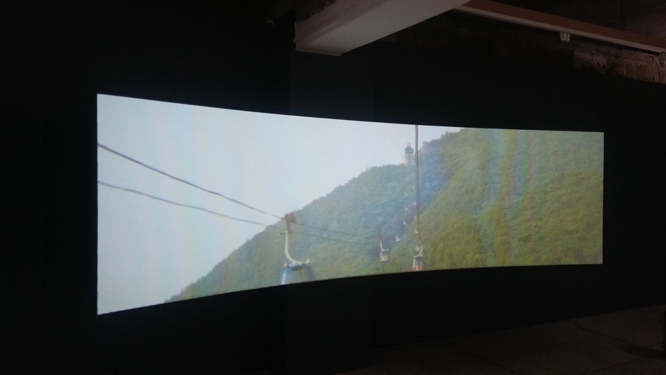 `대양감정'전에 나온 와이드스크린 영상물 `지심도 미륵산'의 일부분. 통영 미륵산 정상과 바닷가를 오르내리는 곤돌라의 행렬에서 시작하는 영상은 불황으로 휘청거리는 거제 조선소, 구조조정에 치인 노동자들의 자살현장, 최근 개발된 관광유흥단지, 지심도 섬과 바다에 깃든 과거 민간인학살의 자취 등을 잇따라 비춘다.