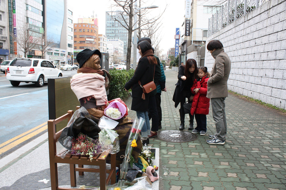 부산 소녀상 방문객 줄이어 부산 동구 초량동 일본영사관 앞 소녀상을 찾는 시민의 발길이 끊이지 않고 있다. 8일 오후 꽃다발과 목도리가 쌓여 있는 소녀상을 찾은 시민들이 주변을 살펴보고 있다.  부산/연합뉴스