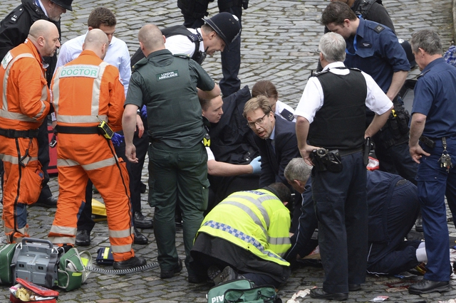 22일 오후 영국 런던의 의사당 인근에서 양복 차림의 토비아스 엘우드 외무차관(가운데)이 구조요원들과 함께 쓰러진 경찰관의 자상 부위를 압박하고 있다. 런던/AP 연합뉴스