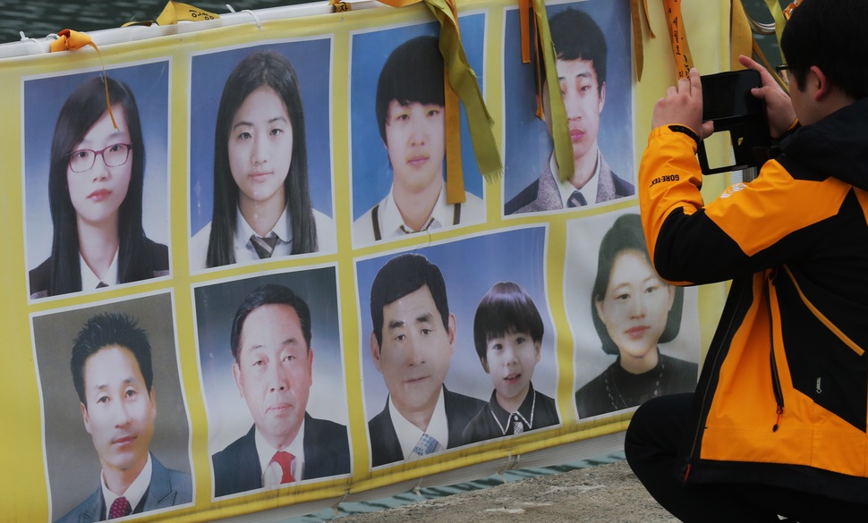 세월호가 인양된 24일 한 추모객이 전남 진도군 팽목항 걸림막에 있는 미수습자 9명의 사진을 휴대전화에 담고 있다. 연합뉴스