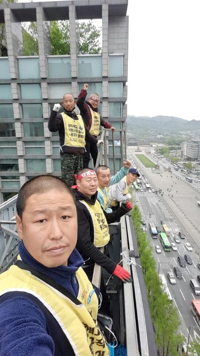 서울 광화문 네거리의 한 빌딩 옥상 전광판 뒤편에서 농성중인 6명의 노동자들이 지난달 17일 사진 촬영을 하고 있다. 맨 앞의 삭발한 남성 장재영(현대차 비정규직 노동자)씨 뒤로 고진수(세종호텔 노동자), 오수일(아사히 비정규직 노동자), 이인근(콜트콜텍 노동자)씨가 차례대로 서 있다. 오수일씨 뒤에는 김경래(삼표동양시멘트 노동자), 김혜진(하이텍알씨디코리아 노동자)씨가 주먹 쥔 손을 위로 뻗은 채 서 있다. 장재영씨 제공