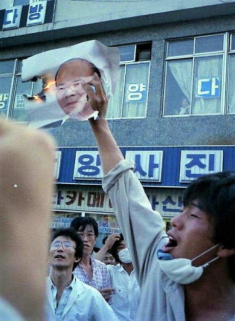 1987년 6월10일 저녁 경남 마산에서 시위에 참여한 한 청년이 양덕파출소에 걸려 있던 전두환 사진을 떼어내 불태우며 구호를 외치고 있다.