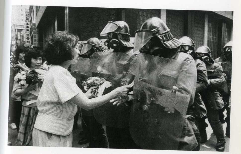 1987년 6월14일 보다 못한 어머니들이 전경들에게 장미꽃을 꽂아주며 최루탄 발사를 중지하도록 부탁하고 있다. 6월민주항쟁계승사업회 사진집
