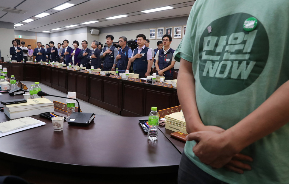 15일 오후 정부세종청사 고용노동부에서 열린 최저임금위원회 제3차 전원회의에서 한 근로자위원이 최저임금 1만원을 촉구하는 옷을 입고 국민의례를 하고 있다. 두차례의 최저임금위 회의는 근로자위원의 불참으로 무산됐고, 3번째 전원회의에 양대 노총이 참석해 사실상 처음 열렸다. 세종/연합뉴스