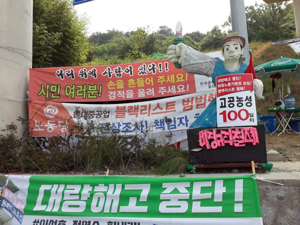 지난 19일 금속노조 현대중공업 사내하청지회가 고공농성장 아래 도로변에 설치한 각종 펼침막과 고공농성 100일을 알리는 조형물. 신동명 기자