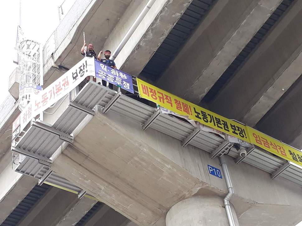 지난 19일 고공농성 100일을 맞은 이성호·전영수(왼쪽부터)씨가 교각 농성장에서 아래쪽을 향해 구호를 외치고 있다. 신동명 기자