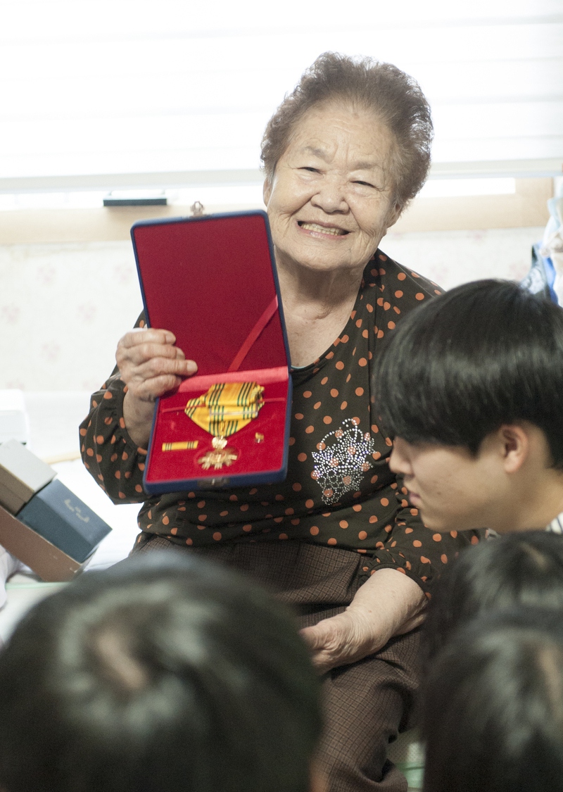 2016년 추석 나눔의 집을 찾아온 ‘김군자할머니기금’ 장학생들에게 김군자 할머니가 훈장(국민훈장 동백장)을 보여주며 웃고 있다. 사진 아름다운재단 제공