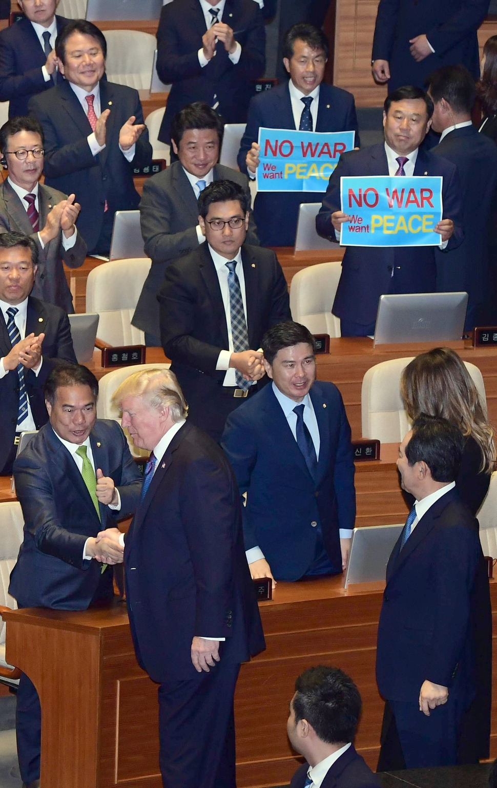 한국을 국빈방문한 도널드 트럼프 미국 대통령이 8일 오전 국회 본회의장에서 연설한 뒤 의원들의 박수를 받으며 퇴장하는 동안 김종훈 민중당 상임대표와 윤종오 원내대표가 ‘전쟁반대, 평화를 원한다’는 내용의 손팻말을 들고 시위를 벌이고 있다. 공동취재사진