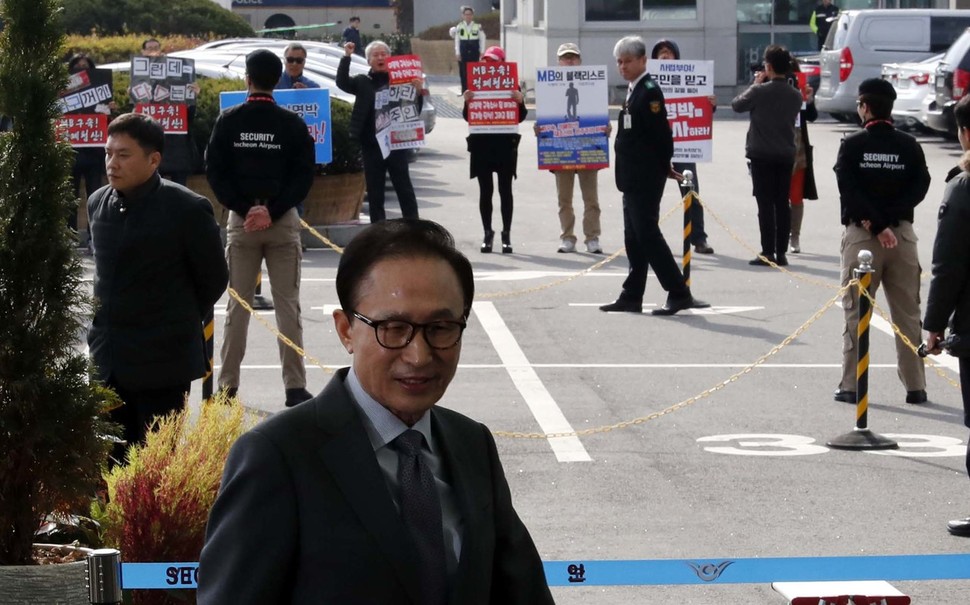 이명박 전 대통령이 12일 낮 인천공항 출국장으로 향하고 있다. 뒤로 이 전 대통령에 대한 수사를 촉구하는 시위대의 모습이 보이고 있다. 인천공항/박종식 기자 anaki@hani.co.kr