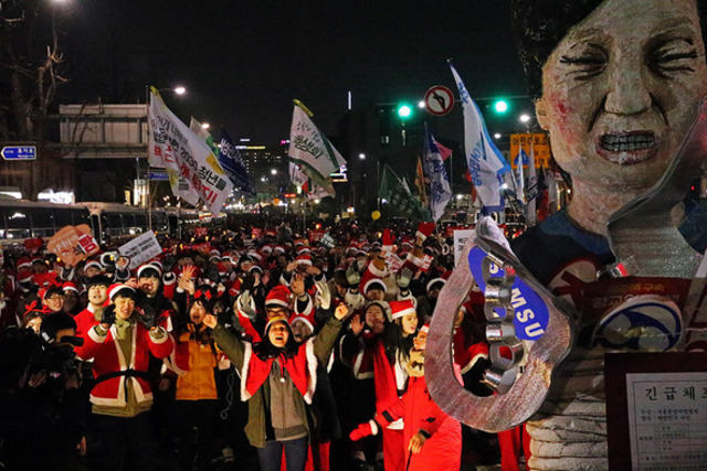 지난해 12월24일 저녁 서울 광화문광장에서 산타클로스 복장을 한 ‘박근혜정권 퇴진 청년행동’ 소속 청년들이 청운효자동주민센터 앞까지 행진해와 박 대통령 모형에 대형 수갑 모형을 건 뒤 환호하는 모습. 김정효 기자 hyopd@hani.co.kr