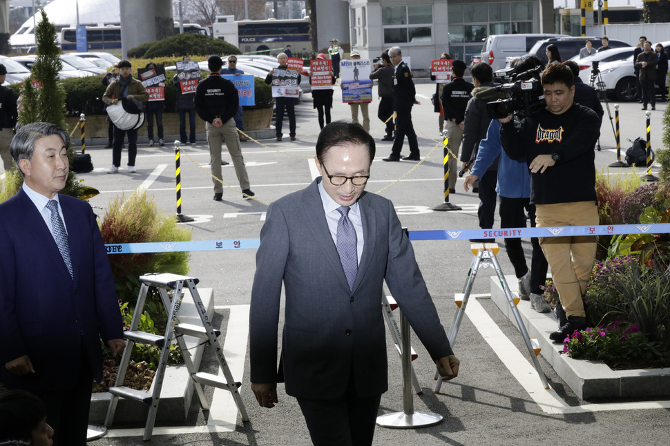 이명박 전 대통령이 지난달 12일 낮 바레인으로 출국하기 위해 인천국제공항 귀빈실로 향하고 있다. 이 전 대통령의 뒤쪽에서 시민사회단체 회원들이 이 전 대통령에 대한 수사를 촉구하는 시위를 벌이고 있다. 인천공항/김명진 기자 littleprince@hani.co.kr