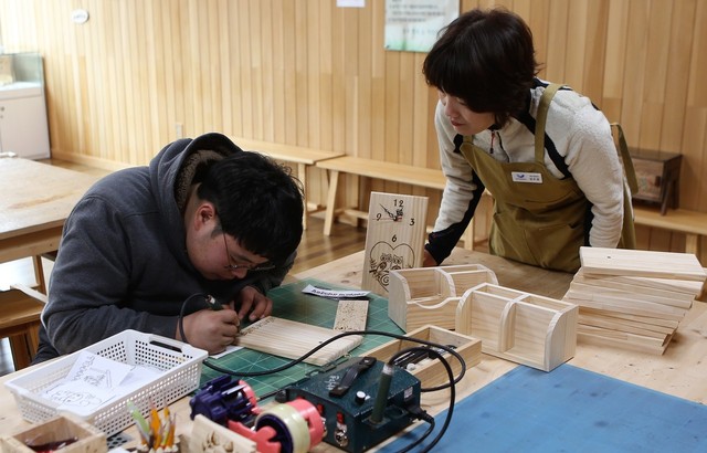 충주 행복숲체험원의 목재문화체험장에서 체험객이 나무판을 이용한 시계를 만들고 있다.